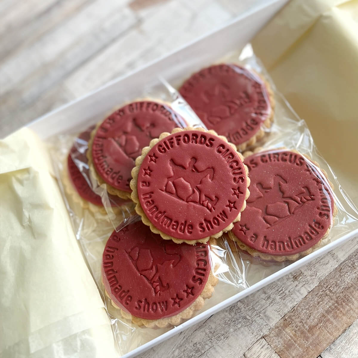 Red cookies with 'Giffords Circus' branding in a clear plastic bag on a wooden surface.