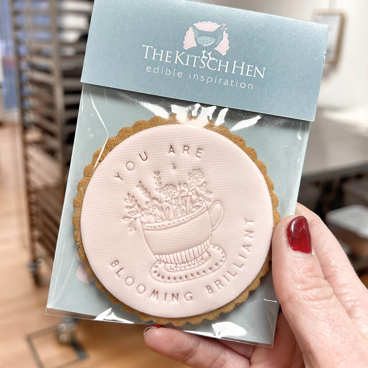 Cookie with 'You are blooming brilliant' message in packaging held by a hand.