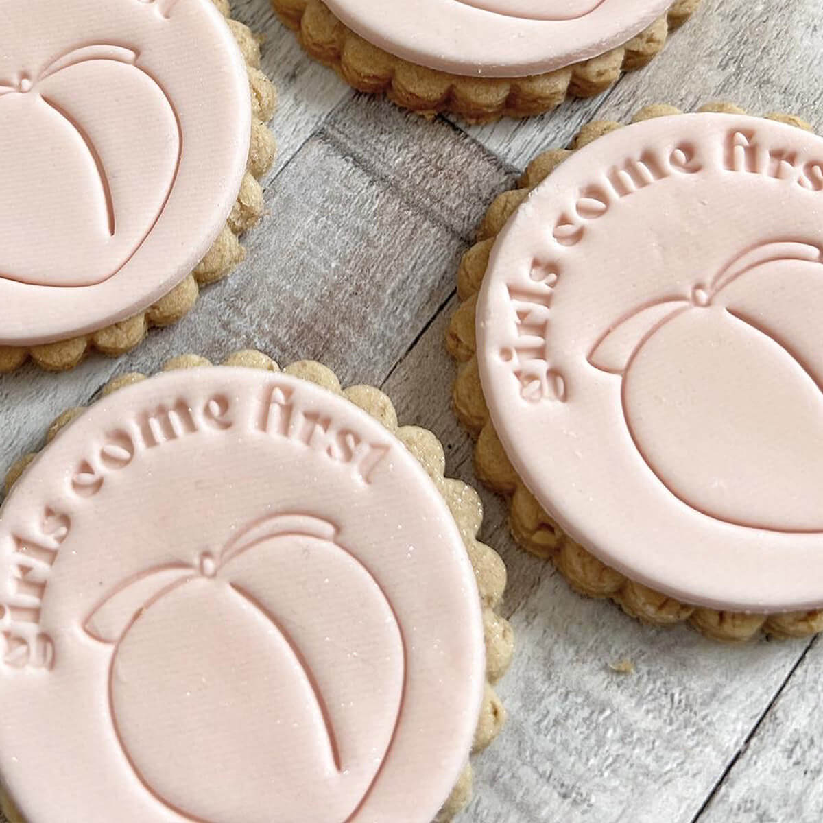 Cookies with pink icing and 'girls come first' text on a wooden surface