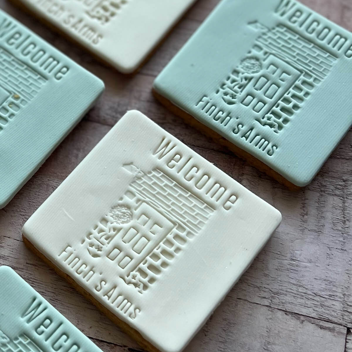 Cookies with 'Welcome' and 'Finch's Arms' embossed on them, arranged on a wooden surface.