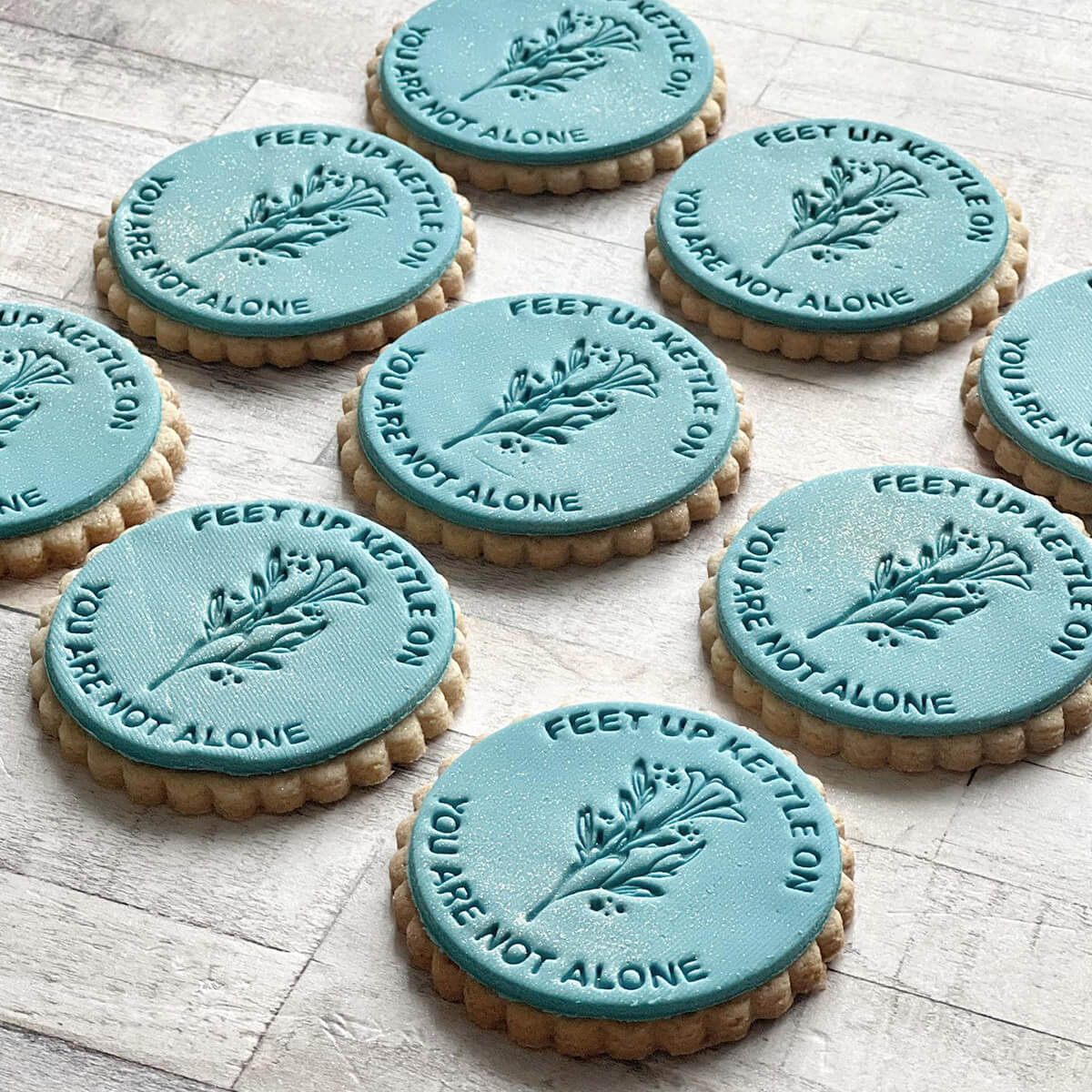 Cookies with teal icing featuring motivational phrases on a wooden surface