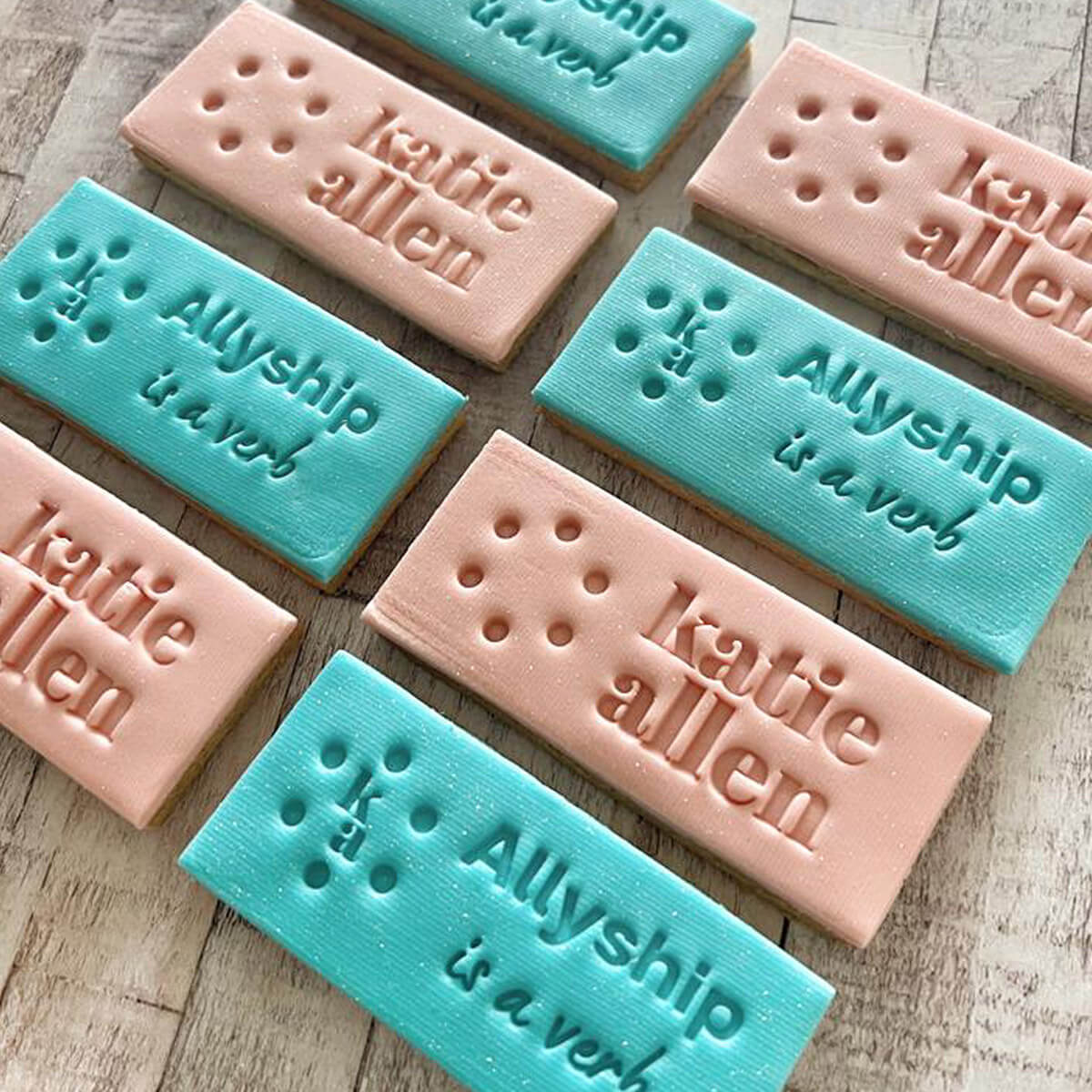 Rectangular cookies with 'katie allen' and 'Allyship is a verb' text on a wooden surface.