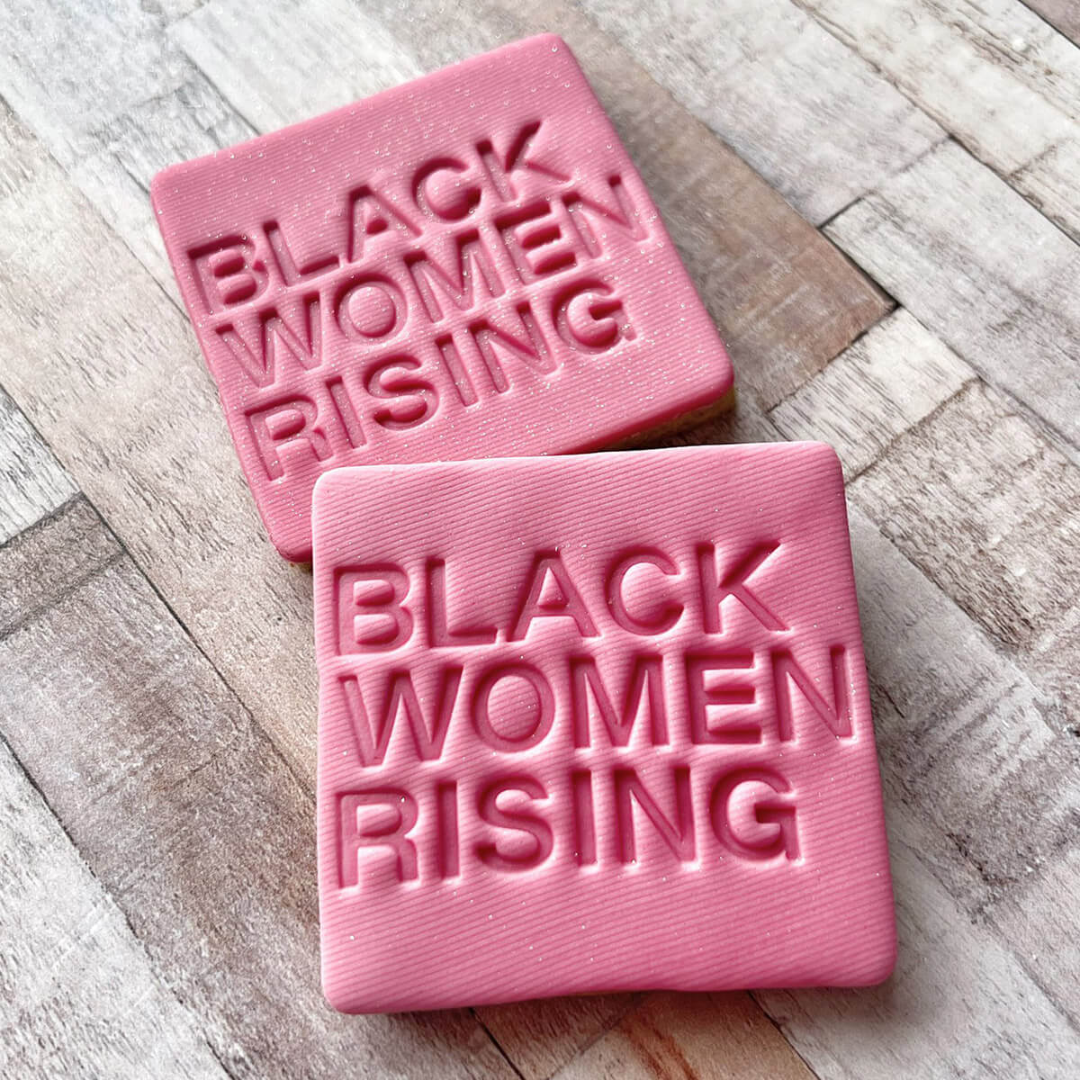 Two pink bars of soap with 'BLACK WOMEN RISING' text on a wooden surface