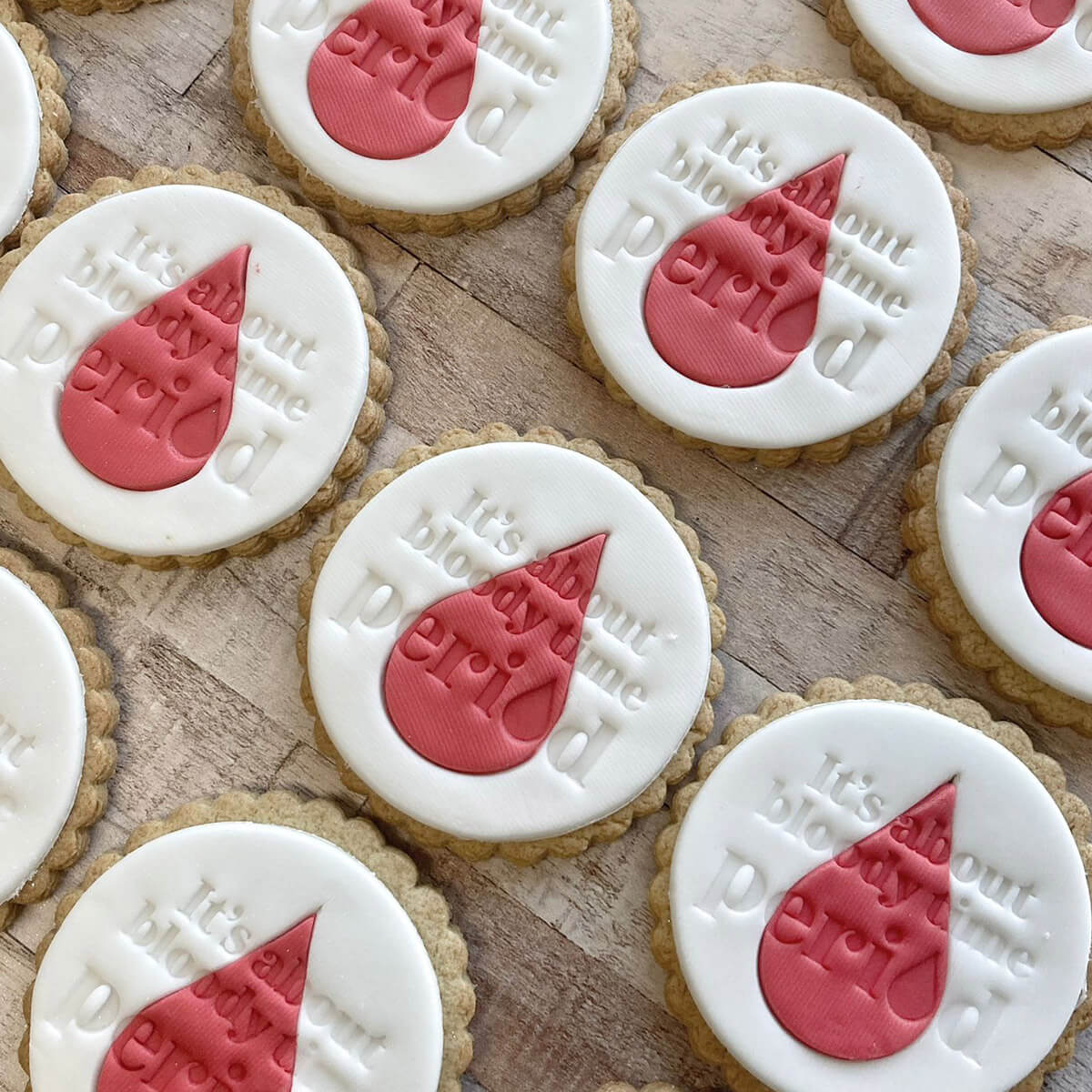 Cookies with white icing and red heart designs saying "It's about bloody time. Period." on a wooden surface