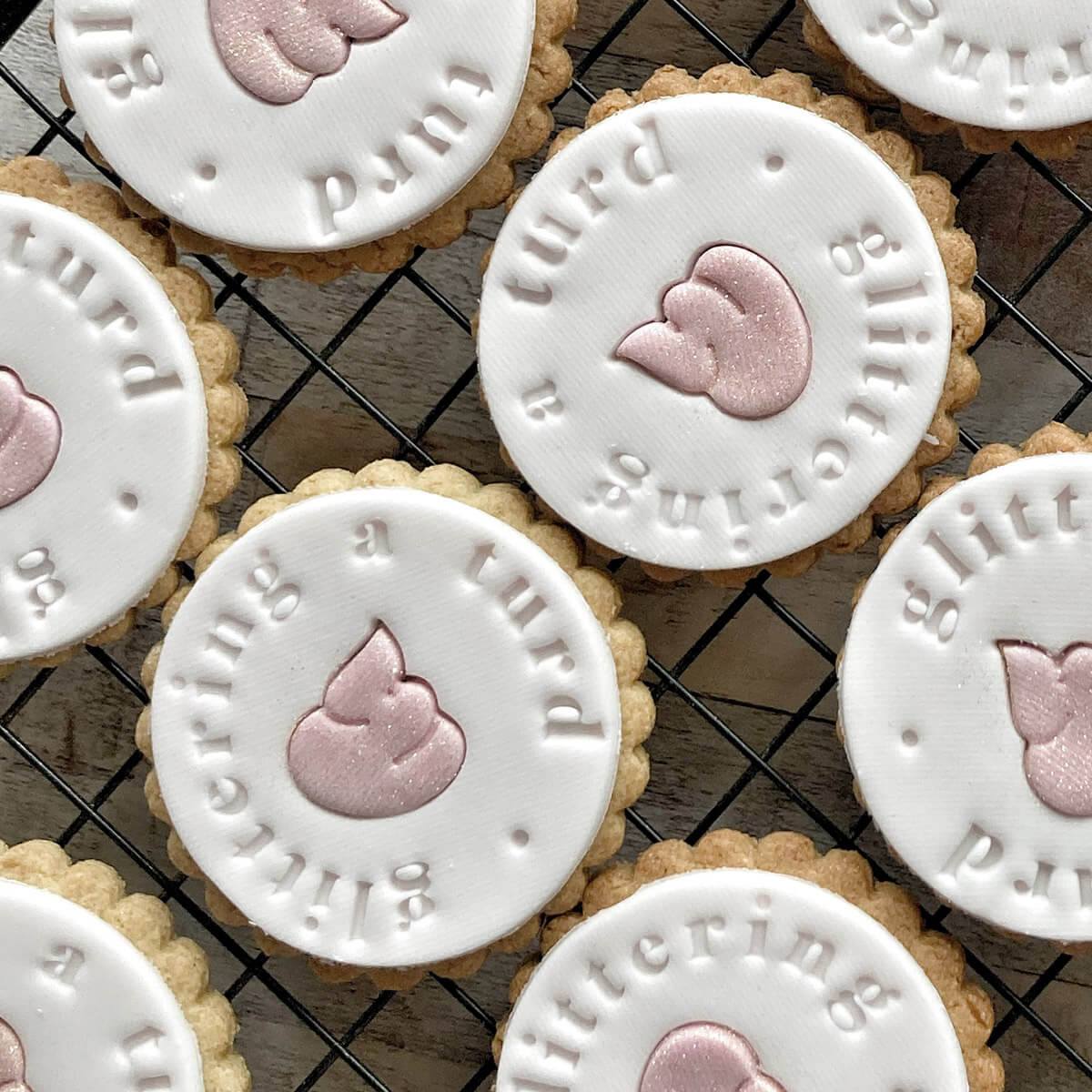 Cookies with white icing and pink poo emoji designs on a cooling rack.